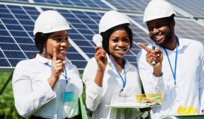 African american technician checks the maintenance of the solar panels. Group of three black engineers meeting at solar station. Hold led bulb.